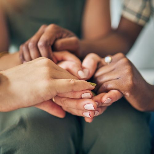 Close-up of diverse hands gently holding each other in a supportive gesture. The scene conveys unity and empathy, with soft lighting enhancing its warmth.